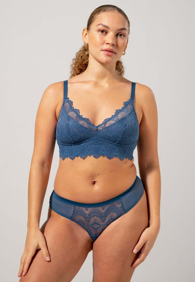 Lace bralette en bijpassende slip in diepblauw. De bralette heeft geschenken randen en verstelbare bandjes; de slip heeft doorzichtige kantpanelen.
