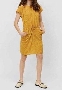 Vestido mostaza con lunares blancos, mangas cortas, cintura fruncida, dos bolsillos frontales y un dobladillo a la altura de la rodilla. Tejido texturizado.