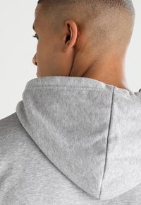 Sweat à capuche gris en tissu doux et texturé avec une capuche volumineuse, vu de dos, avec une doublure de cou sans couture et aucun logo visible.