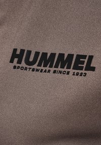 Brown fabric features a textured surface with a prominent black logo reading "HUMMEL" and "SPORTSWEAR SINCE 1923" in bold lettering.