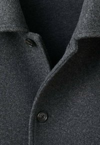 Cappotto di lana grigio con colletto a rever, tessuto strutturato e dettaglio con bottoni neri. Il design enfatizza calore e struttura.