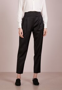 Czarne spodnie z wysokim stanem, z zakładkami, wykonane z gładkiego materiału. Projekt wyróżnia się zwężającymi się nogawkami i jest zestawiony z białą koszulą na guziki.