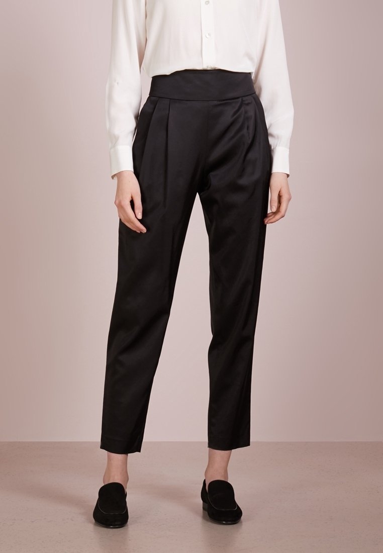 Czarne spodnie z wysokim stanem, z zakładkami, wykonane z gładkiego materiału. Projekt wyróżnia się zwężającymi się nogawkami i jest zestawiony z białą koszulą na guziki.