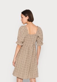 Vestido curto bege com mangas bufantes, costas quadradas, tecido texturizado e padrão xadrez. Apresenta uma cintura franzida e uma saia fluida.