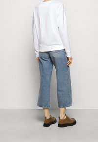 Sudadera blanca de corte relajado, combinada con jeans de pierna ancha en azul claro. Zapatos marrones con suelas negras complementan el conjunto.
