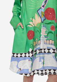 Vestido verde con estampados coloridos de flores y cisnes, con un bolsillo en el lado izquierdo y un borde estampado en negro y azul.