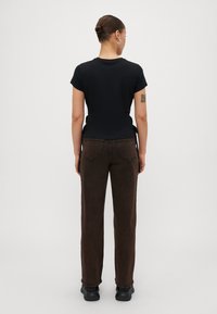 Zwarte T-shirt met korte mouwen in combinatie met bruine high-waisted broek. De outfit heeft een eenvoudige snit, is van katoen gemaakt en heeft een ontspannen pasvorm, gedragen met zwarte schoenen.