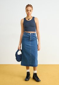 Blue denim midi skirt with front button, paired with a dark tank top. Black high-top sneakers and a textured blue handbag complete the look.