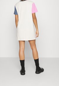 Vestito a maniche corte a blocchi di colore beige, rosa e blu. Realizzato in tessuto morbido, lunghezza al ginocchio con vestibilità ampia, abbinato a calzini e scarpe nere.