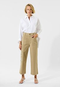 Witte overhemd met knoopsluiting, gecombineerd met beige hoge taille wijde broek met zijzakken en bloemmotieven.