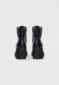 Zwarte leren enkelboots met een gestructureerde hak, ritssluiting en zachte voering. Licht afgeronde neus en een stevige, ribbelige hak.