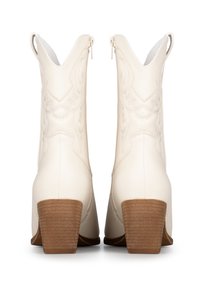 Botas de cowboy color crema hechas de cuero texturizado, con un tacón de madera apilada y costuras decorativas a lo largo de la parte trasera.
