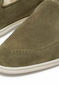 Green suede slip-on shoes with a rounded toe and contrasting white rubber sole. Features minimal stitching and a smooth texture.