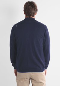 Pull en tricot bleu marine à manches longues et ourlet côtelé, avec un détail de logo subtil sur l'épaule et une texture lisse.
