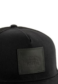 Czarna czapka wykonana z teksturowanej tkaniny, z kwadratową skórzaną łatą z wypukłym logo. Projekt panelu z zaokrągloną koroną.