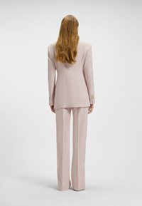 Hellrosa maßgeschneiderter Anzug mit einreihigem Blazer und weitem Bein, gefertigt aus glattem Stoff mit strukturiertem Sitz.