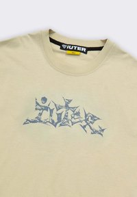 T-shirt beige con collo a giro, con un logo grafico blu consumato e un'etichetta nera e gialla che indica la taglia small.