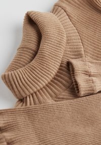 Tissu côtelé marron clair avec une texture douce, doté d'un col replié et de détails au niveau des poignets, créant une apparence superposée.