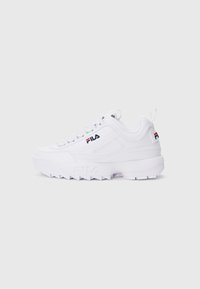 Baskets basses blanches FILA avec semelle épaisse, logo sur le côté et le talon, et fermeture à lacets sur un fond clair.