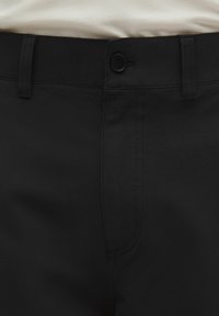 Pantaloni neri realizzati in tessuto liscio con un design aderente. Presentano una vita piatta, tasche laterali e una chiusura con bottone.