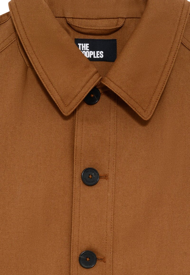 Veste marron à boutonner avec col évasé, boutons noirs et tissu texturé avec de subtils détails de couture. L'étiquette de la marque est visible.