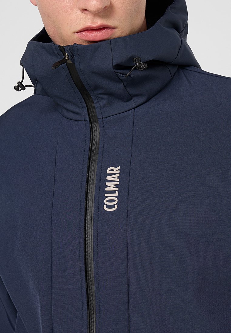 Navyblaue Kapuzenjacke mit Reißverschluss, aus strukturiertem Stoff und mit der Marke "COLMAR" in hellen Buchstaben auf der Vorderseite.
