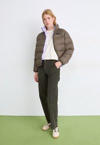 Bruine en beige pied-de-poule pufferjas met paarse voering, gecombineerd met olijfgroene broek en beige sneakers met bruine strepen. Gladde textuur.