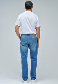 Vaqueros de mezclilla azul con corte recto, bolsillos visibles y un lavado claro. Combinados con una camiseta blanca básica y zapatillas blancas.
