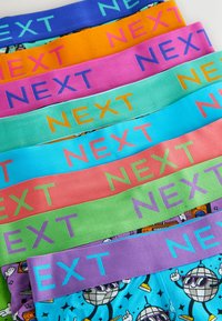 Různé boxerky s barevnými pásy označenými nápisem "NEXT", v jasných barvách jako modrá, oranžová, růžová, zelená a s vzory na tkanině.