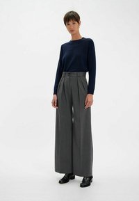Haut à manches longues bleu marine associé à un pantalon à jambes larges gris rayé avec des plis et une fermeture à bouton sur le devant. Des bottines noires à la cheville complètent l'ensemble.
