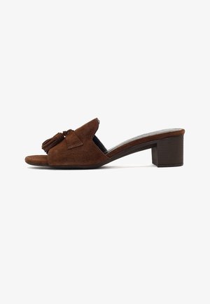 Mule aperto sulla punta in pelle scamosciata marrone con tacco a blocco e nappine decorative sulla parte superiore, vista laterale su sfondo bianco.