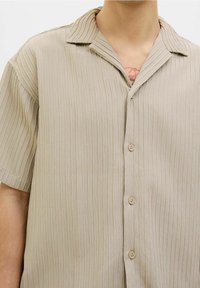 Beige shirt met korte mouwen en een gestructureerd, geribbeld patroon, voorzien van een ingesneden kraag en vijf knopen aan de voorkant.