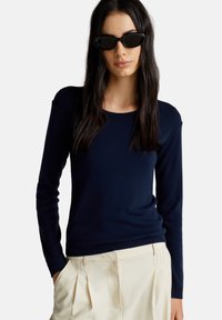 Granatowy sweter dzianinowy z długim rękawem i okrągłym dekoltem, w połączeniu z jasnymi, plisowanymi spodniami. Gładka tekstura z dopasowanym fasonem.