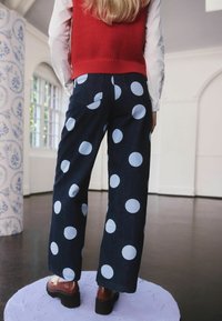 Denim bővülő nadrág nagy világoskék pöttyökkel, magas derékkal és hátsó zsebekkel, piros kötött mellénnyel és barna platform cipőkkel párosítva.