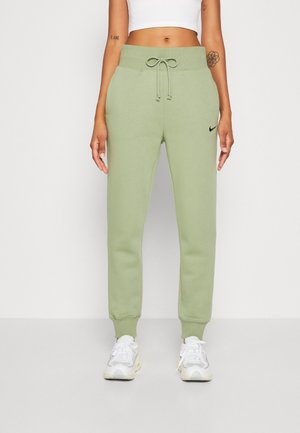 Person iført lysegrønne Nike joggers med snøre i taljen, hvide sneakers og en cropped hvid top mod en ensfarvet baggrund.
