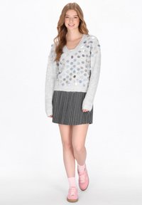 Szary, dzianinowy sweter z kolorowymi cekinami, połączony z ciemną, plisowaną spódnicą. Różowe trampki i skarpetki dopełniają stylizację.