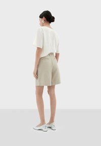 Witte korte mouwen top, khaki korte broek en zilveren schoenen. De top heeft een losse pasvorm; de shorts zijn op maat gemaakt met zakken; gladde textuur.