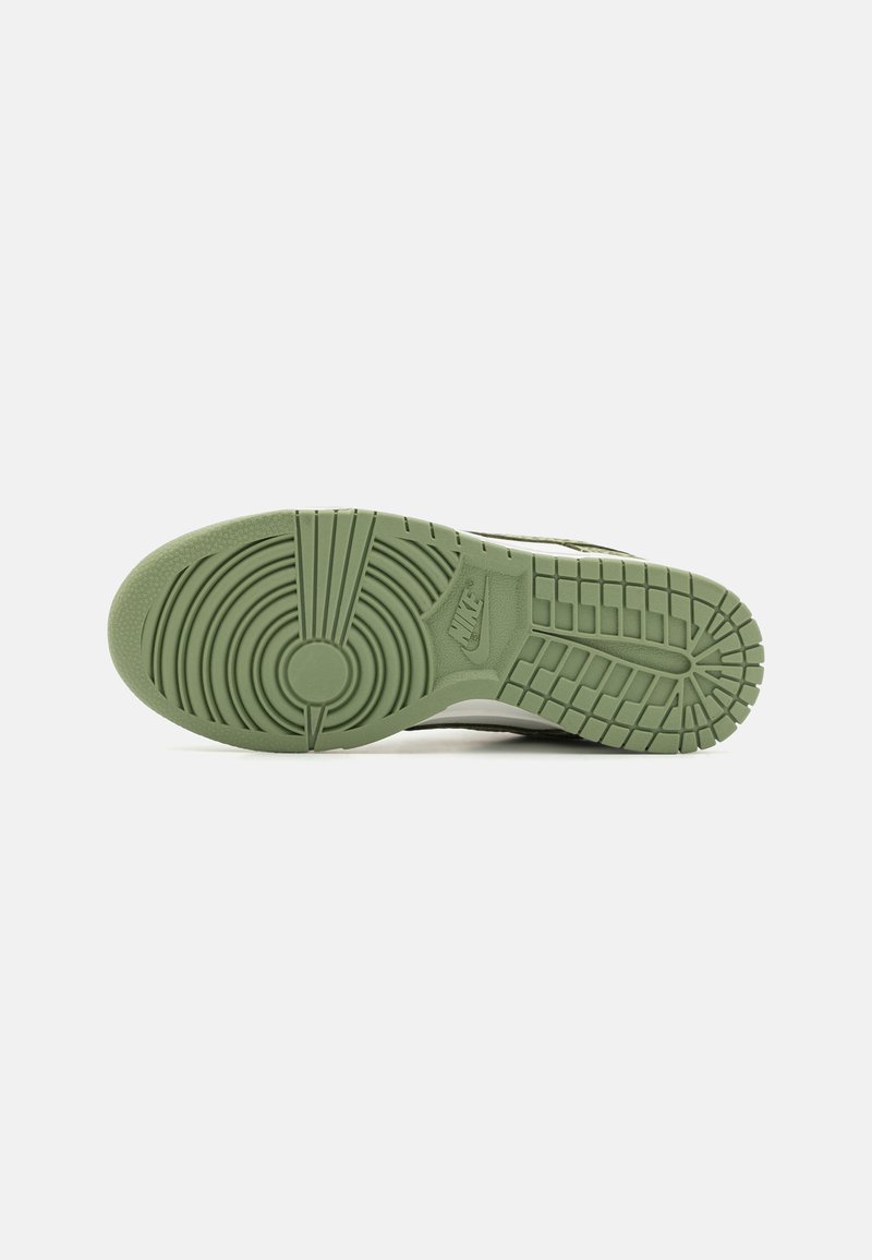 Baskets Nike avec une semelle en caoutchouc vert texturé, présentant des motifs circulaires et un logo bien visible, vues du dessous.