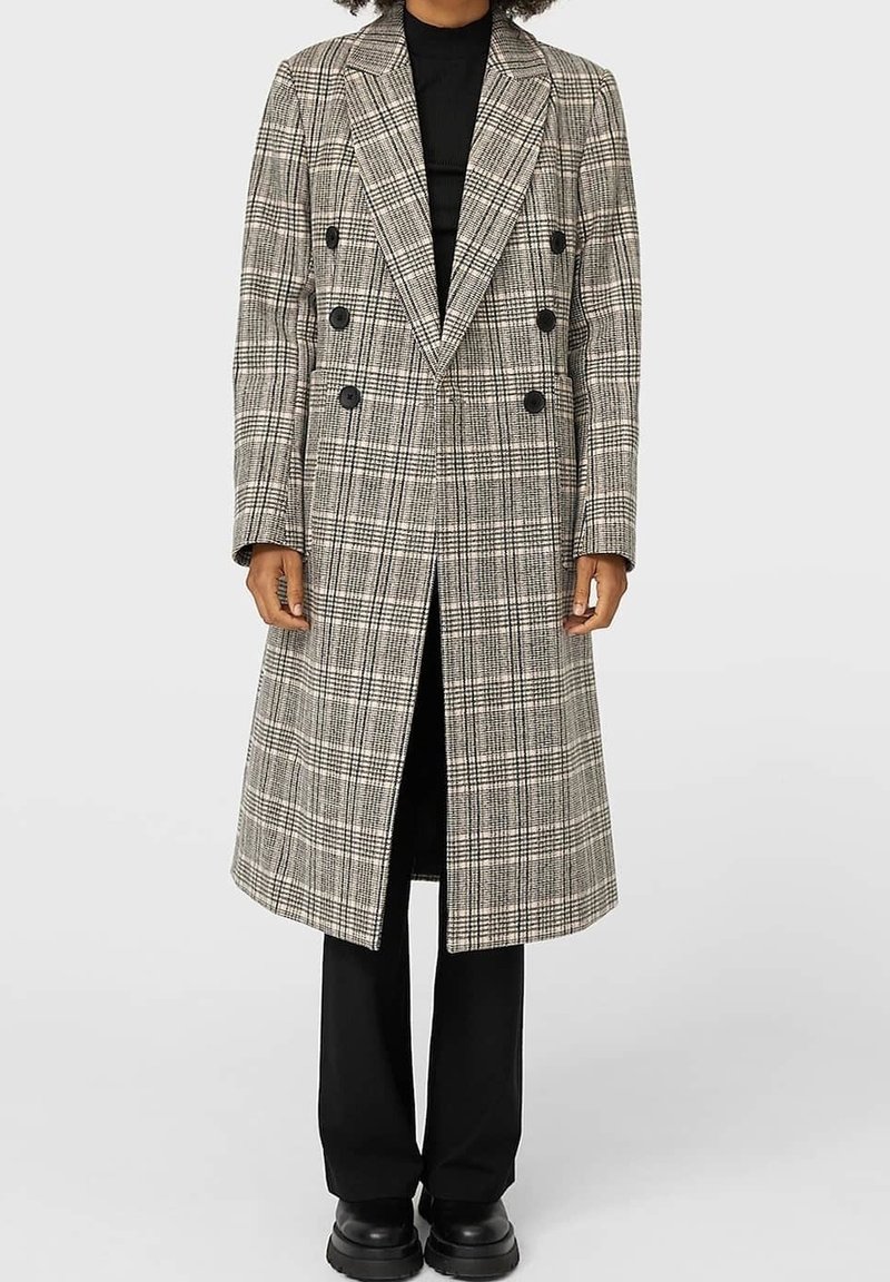 Abrigo de cuadros en gris y negro, de doble botonadura; cuenta con botones grandes, solapas pronunciadas y un diseño hasta la rodilla, con una textura suave.