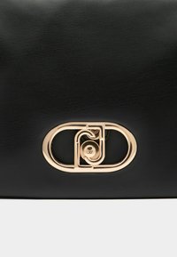 Borsa a mano in pelle nera con chiusura ovale color oro con un design geometrico unico. Superficie testurizzata senza motivi visibili.