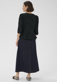 Schwarze Bluse mit Struktur, dreiviertellangen Ärmeln und Peplum-Saum, kombiniert mit einem dunklen Jeans-Maxirock und schwarz-weiß gestreiften Ballerinas.