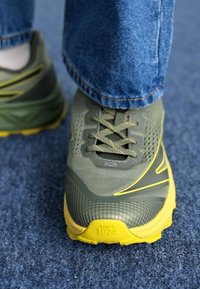 Grüne und gelbe Sportschuhe mit Mesh-Obermaterial, strukturierten Oberflächen und flachen Schnürsenkeln. Mit Logo und "SEIT 1974" auf der Sohle.