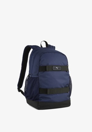 Granatowy plecak Puma z czarnymi paskami, siateczkowymi bocznymi kieszeniami, wyściełanymi paskami na ramiona i zamykanym na zamek głównym komorą.