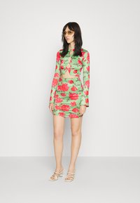 Top cropped de manga longa verde com flores e rosas vermelhas, combinado com uma saia mini a condizer. Apresenta detalhes recortados e um corte ajustado.