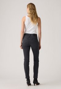 Jeans de denim negros ajustados con dos bolsillos traseros, detalles de costura sutiles y una cintura de altura media, combinados con una camiseta sin mangas blanca.