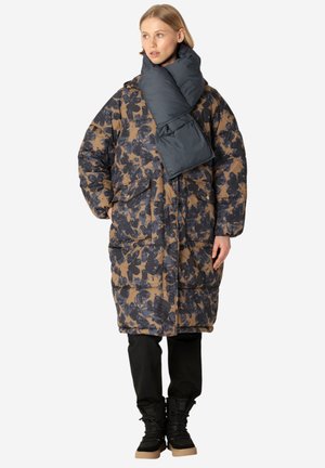 Gevoerde jas met een donker bloemenpatroon in marineblauw en bruin. Beschikt over een afneembare donkere sjaal, voortassen en een relaxte silhouet. Zwarte broek en laarzen.