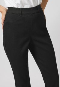 Pantalones de mezclilla negros con un diseño ajustado, que cuentan con una cintura alta, bolsillos laterales y detalles de costura visibles. Textura suave y color clásico.