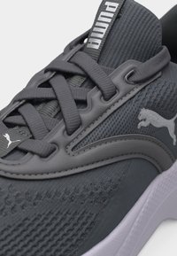 Κοντινό πλάνο σκούρου γκρι αθλητικού παπουτσιού Puma με υφασμάτινο επάνω μέρος με υφή, ενσωματωμένο σύστημα κορδονιών και λευκή σόλα. Το λογότυπο Puma είναι εμφανές στο πλάι και στη γλώσσα.