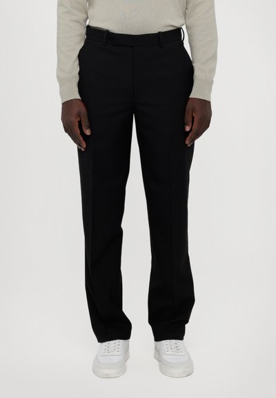 Pantalones negros a medida, hechos de una tela suave, con un diseño de pierna recta y lazos para cinturón, combinados con zapatillas blancas.
