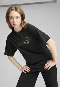 Sort oversized T-shirt lavet af bomuld, med et farverigt "PUMA" logo grafik. Korte ærmer og en afslappet pasform, parret med sorte bukser.